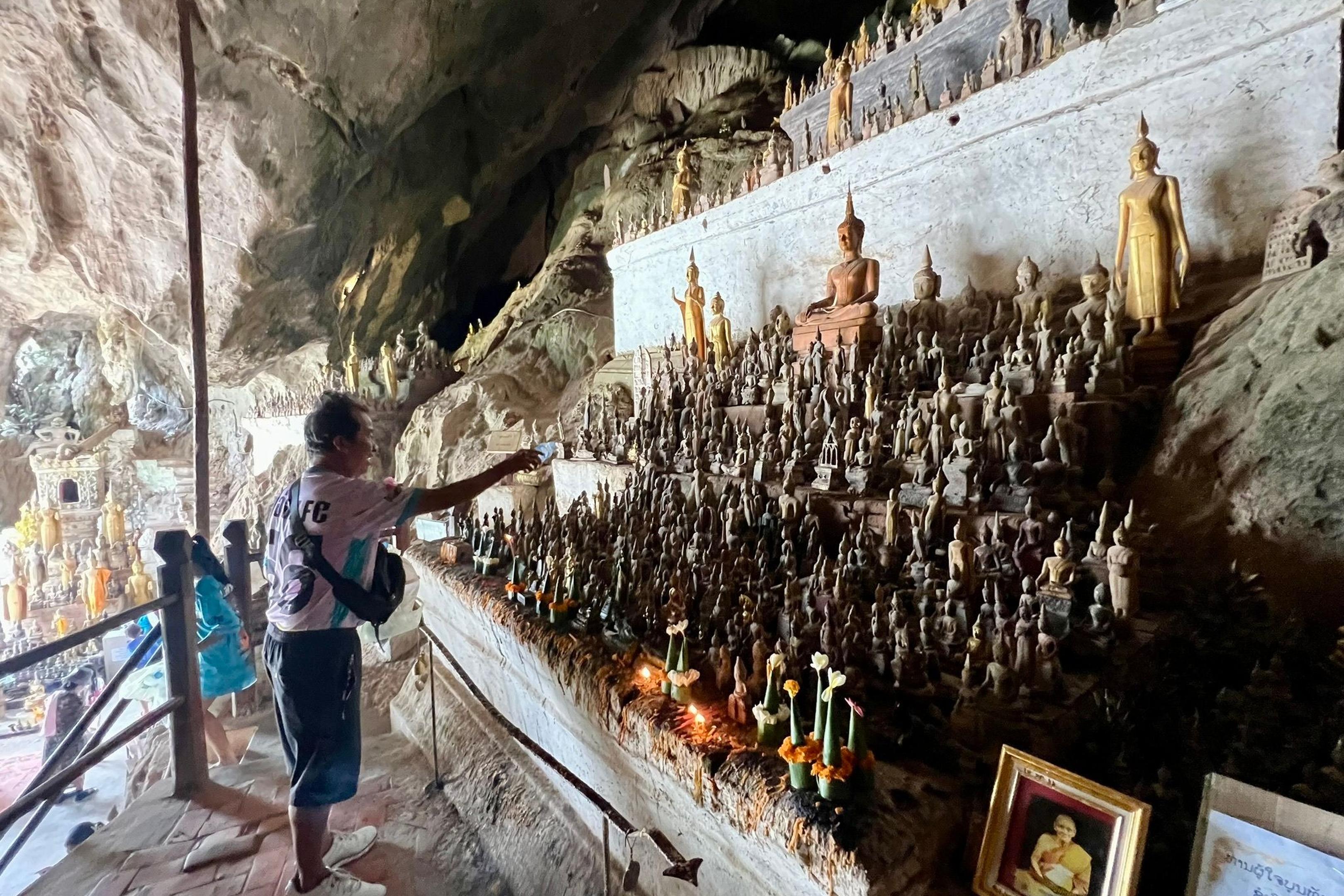 Ein Mann besprenkelt Buddha-Statuen in den Pak Ou Caves als Zeichen des tiefen Respekts mit Wasser.
