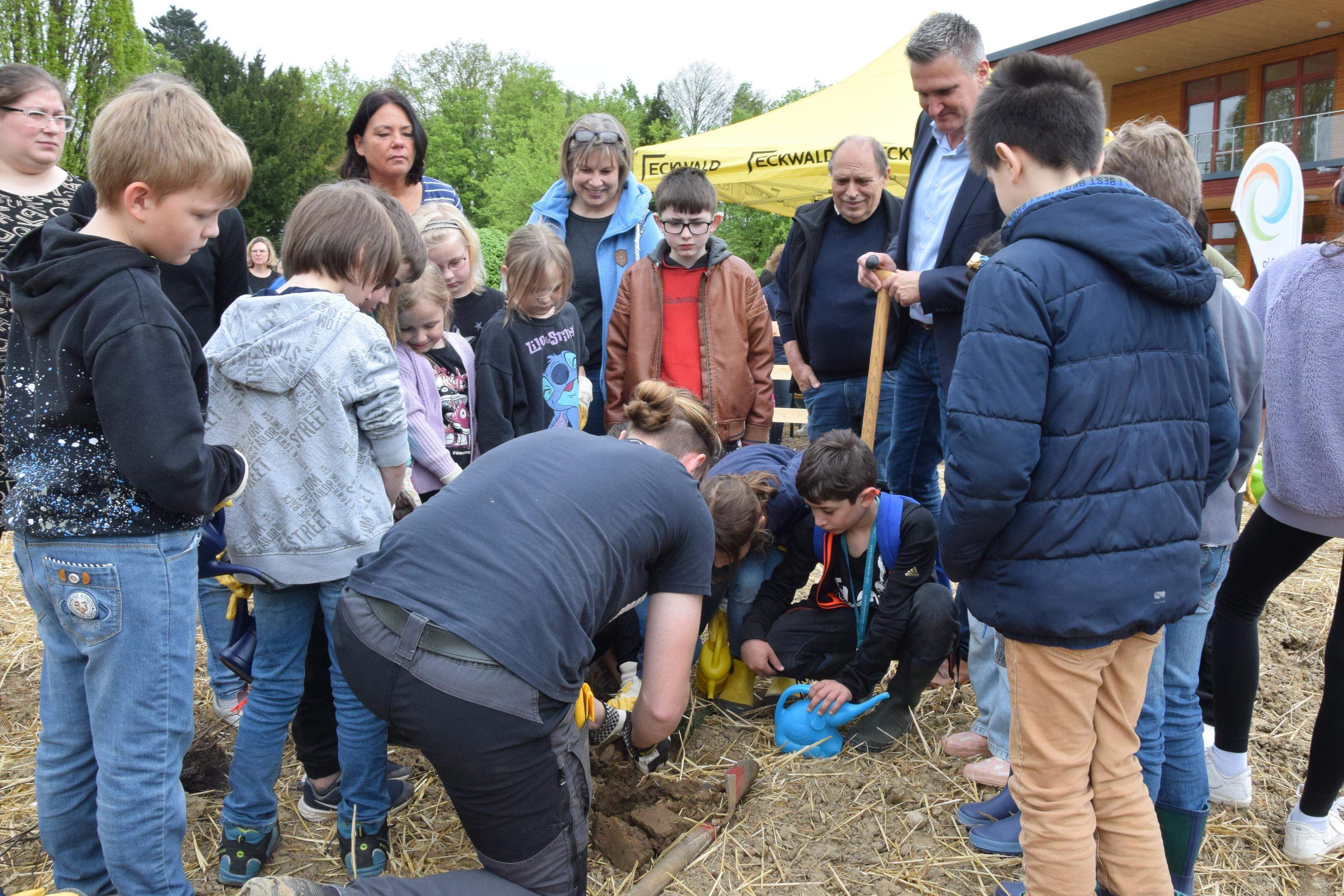 Ein Forstexperte erklärt den Kindern der OGS Niederzier im Beisein von Bürgermeister Frank Rombey, wie sie die Bäume und Sträucher in die Erde pflanzen sollen.