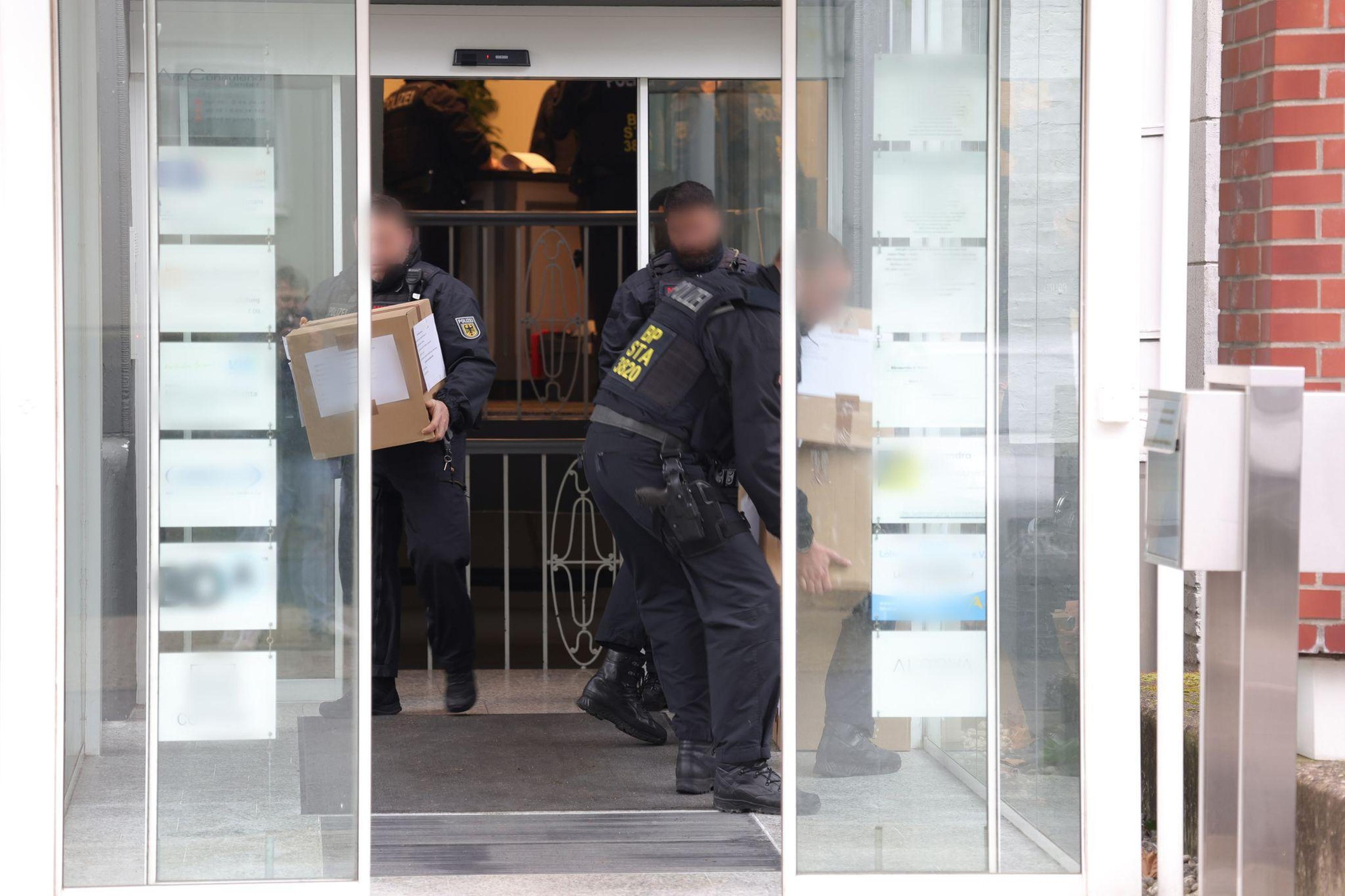  Polizeibeamte tragen bei der Razzia in Kartons sichergestelltes Material aus einem Gebäude.