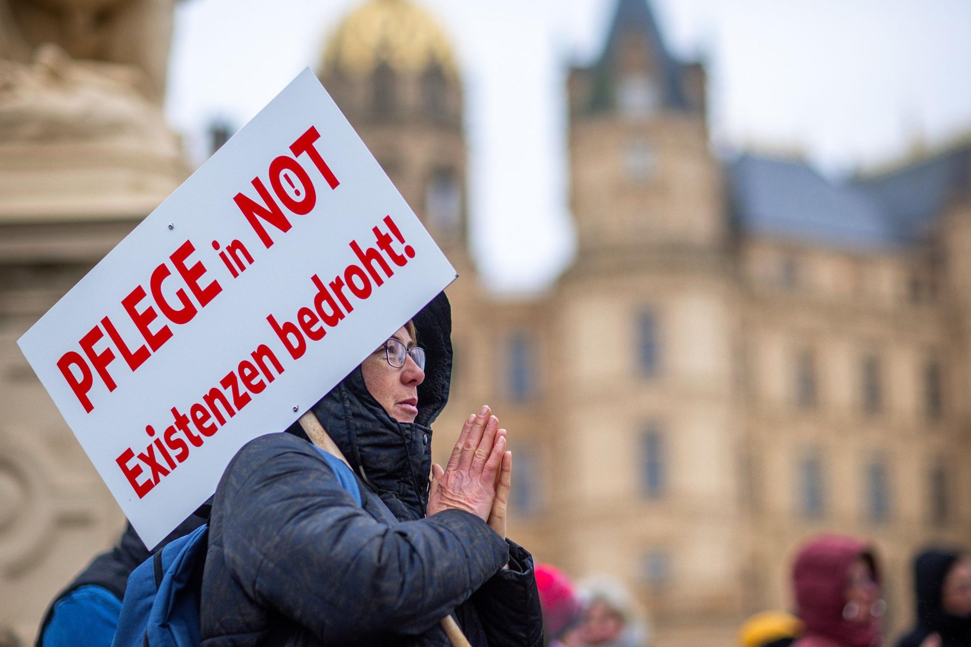Bei einer Protestaktion vor dem Schweriner Landtag hält eine Teilnehmerin ein Schild mit der Aufschrift „Pflege in Not - Existenzen bedroht!“.