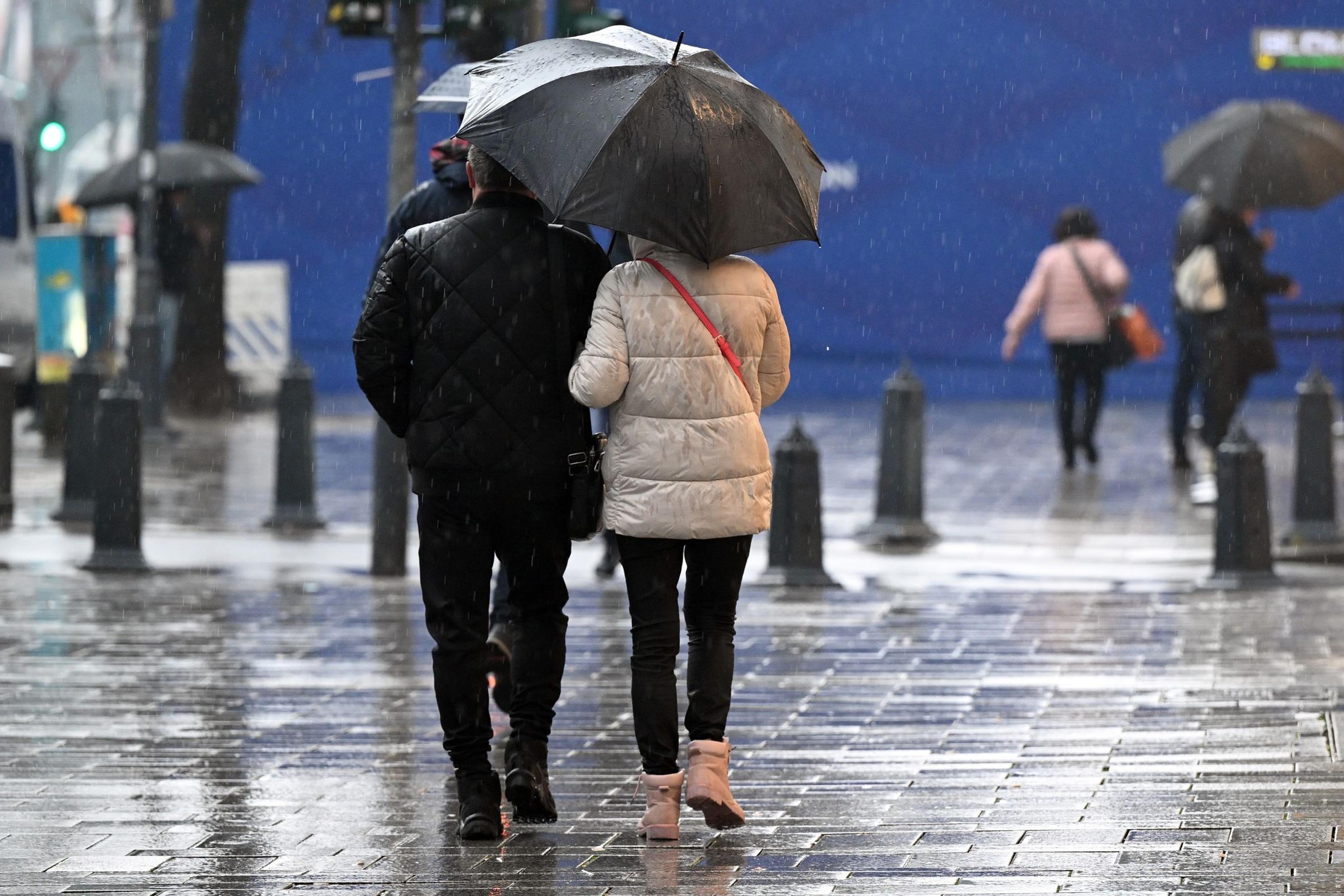 Passanten gehen bei Regen durch eine Fußgängerzone in Düsseldorf.