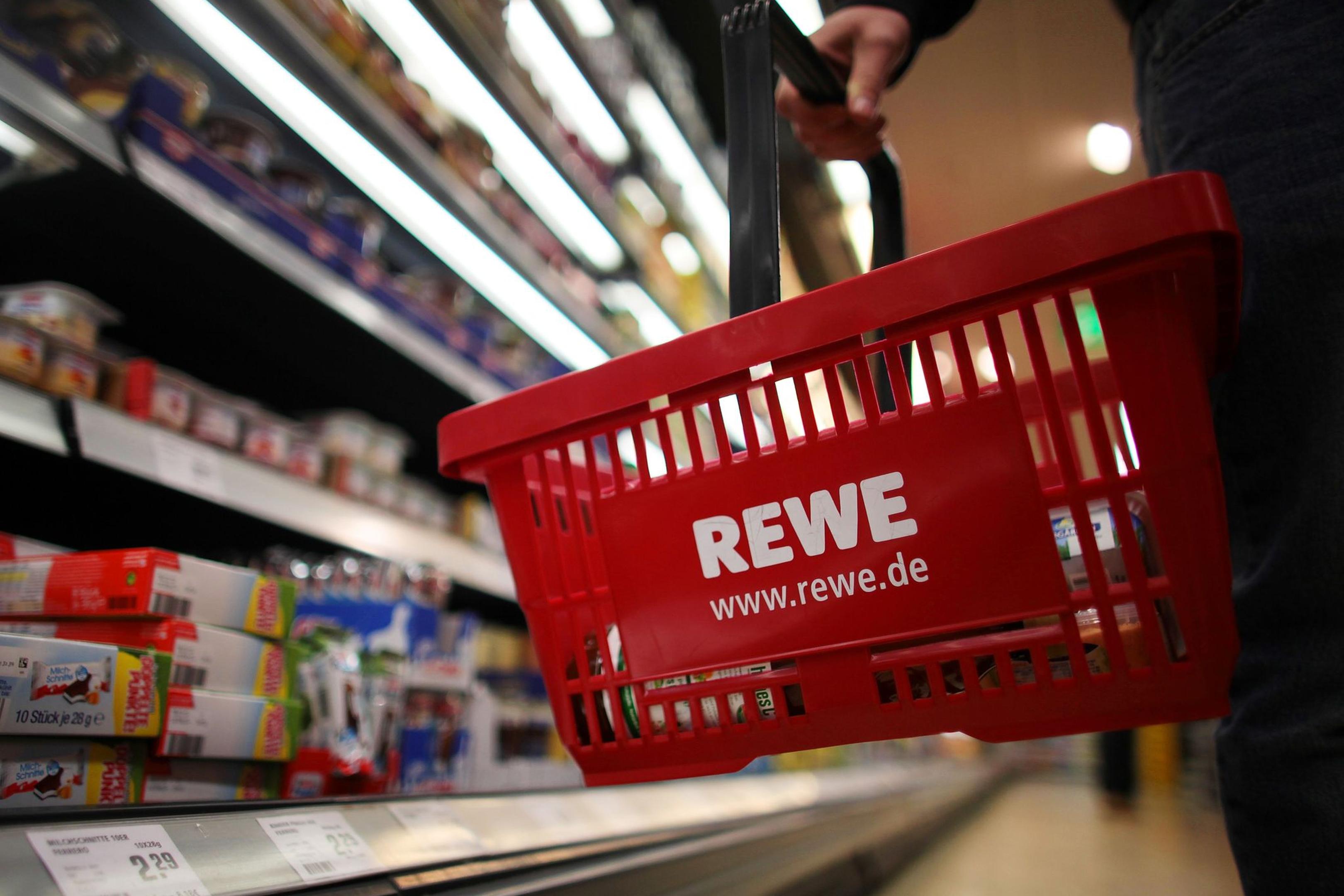 Ein Kunde geht in Köln in einem Rewe-Supermarkt mit einem Einkaufskorb am Kühlregal entlang.